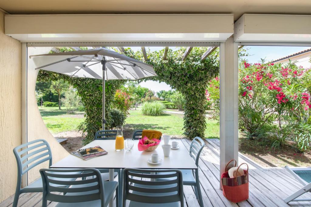 a table and chairs on a porch with an umbrella at SOWELL RESIDENCES Les Sablons in Le Grau-du-Roi