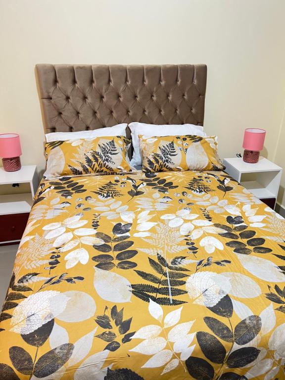 a bed with a yellow and white comforter and pillows at Hibiscus Apartments in Ndola