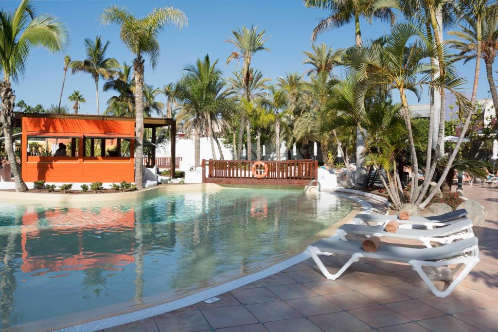 a pool at the resort with two lounge chairs and palm trees at Hotel Gran Canaria Princess - Adults Only in Playa del Ingles