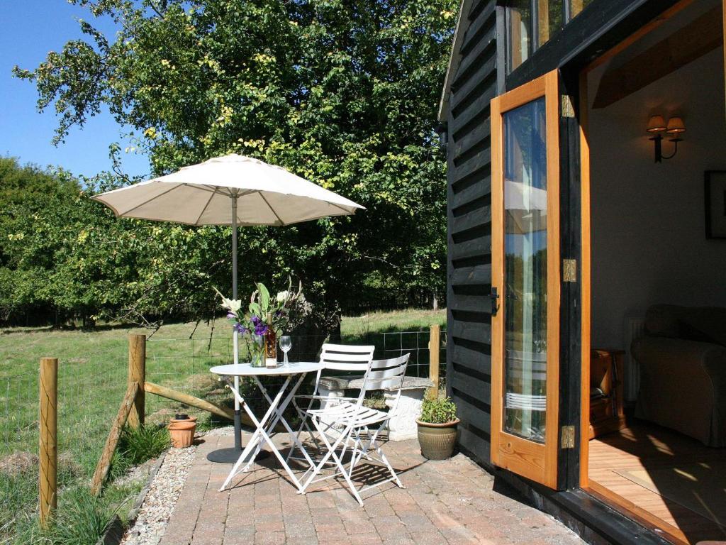 eine Terrasse mit einem Tisch, Stühlen und einem Sonnenschirm in der Unterkunft The Barn At Fishponds in Brook