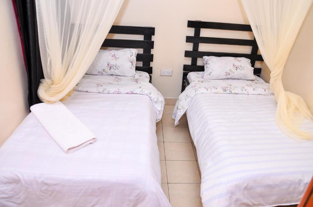 two beds in a room with white sheets at Milany Homes - NEAR JKIA AIRPORT in Nairobi