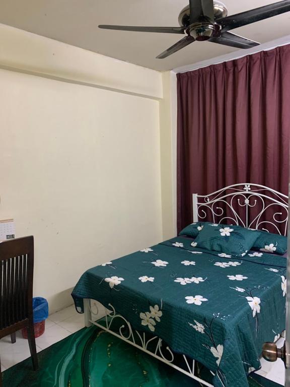 een slaapkamer met een bed met een groene deken en een plafondventilator bij JoeRos Homestay in Shah Alam