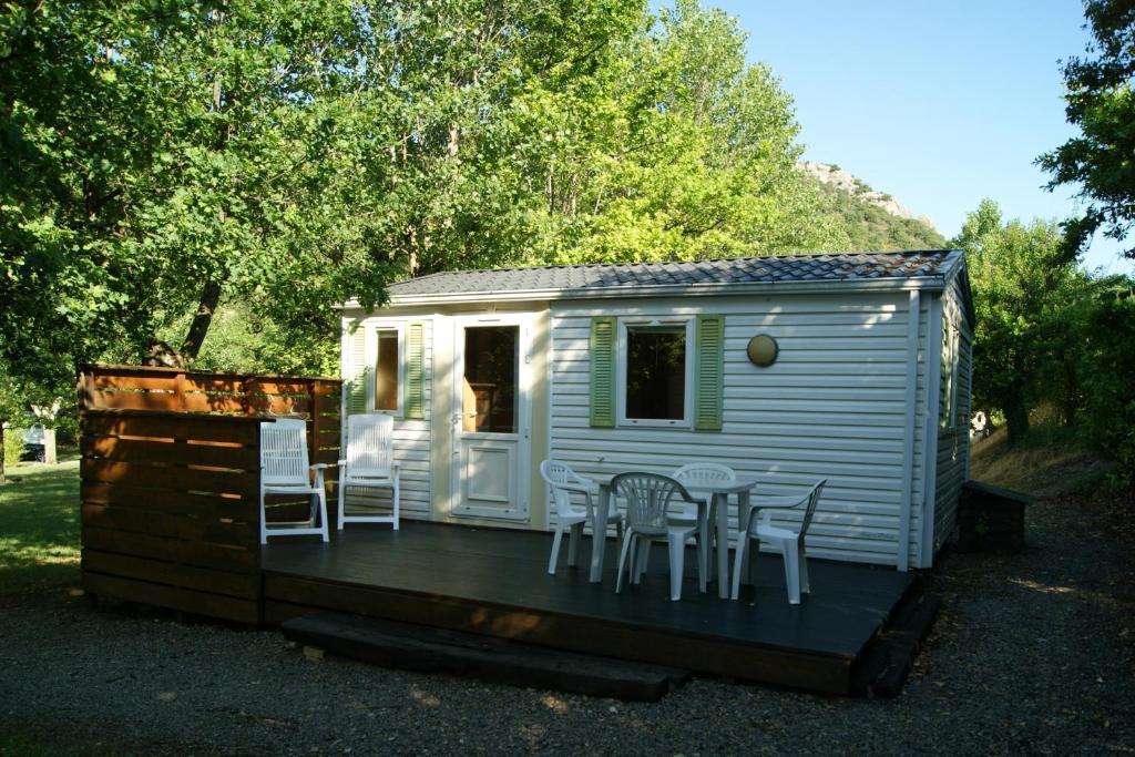 Cabaña blanca con sillas y mesa en la cubierta en Camping le Chambron, en Condorcet