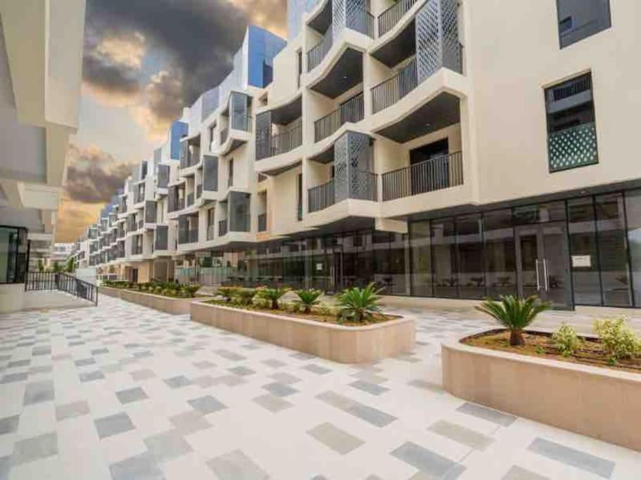a large building with a courtyard in front of it at Lovely New 1 bed Apt - Mirdif Hills Avenue in Dubai