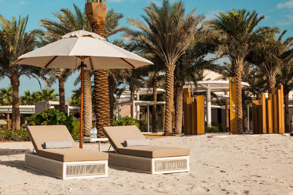 two chairs and an umbrella on a beach with palm trees at ERTH Abu Dhabi Hotel in Abu Dhabi