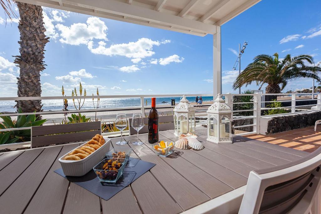 a table with a bottle of wine and food on a deck with the beach at Casa La Malondra in Puerto del Carmen