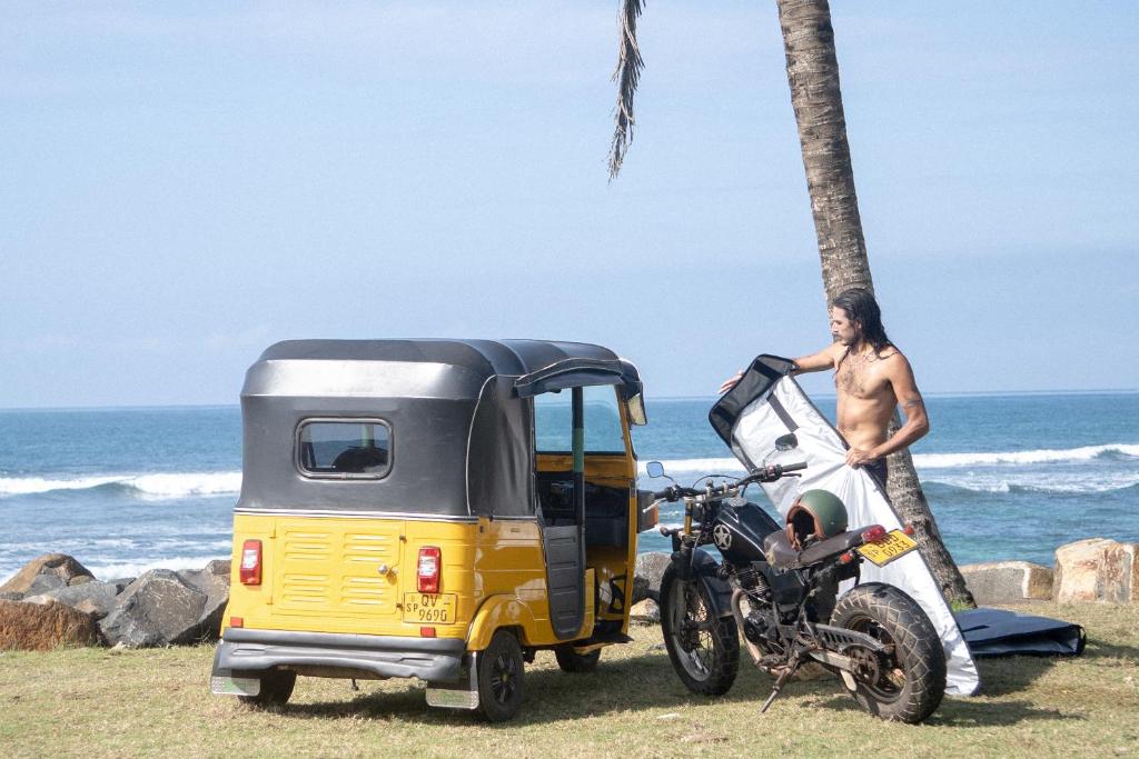a man standing next to a motorcycle next to a tiny caravan at Lotus Surf And Wellness in Ahangama