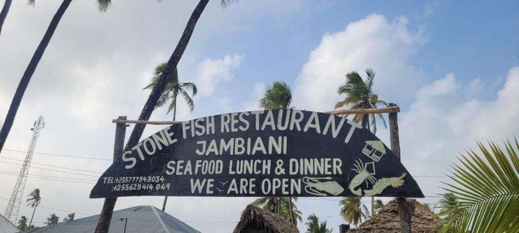 un cartello per un ristorante su una spiaggia con palme di Stonefish Inn Jambiani a Jambiani