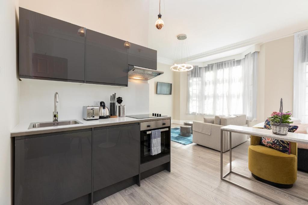 a kitchen with black cabinets and a living room at Air Conditioned Apt High St Kensington in London