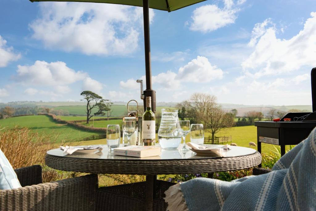 a table with wine glasses and an umbrella on a field at Linhay at East Trenean Farm -Luxury retreat for 2 with stunning rural views, private hot tub and EV charging in Looe