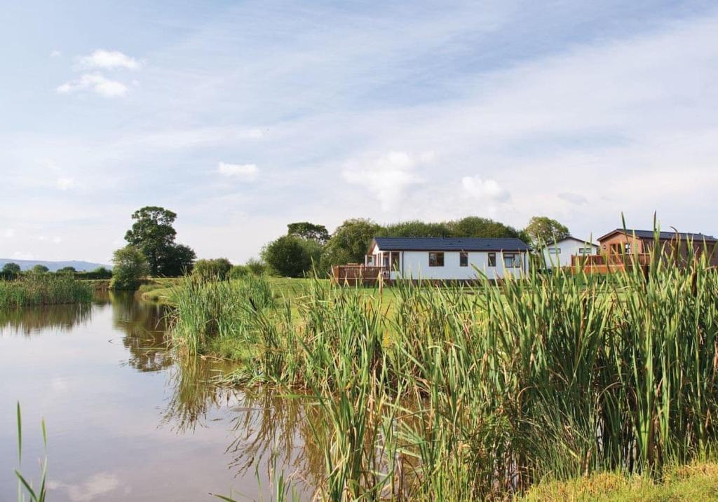 una casa en un campo junto a un cuerpo de agua en Wigmore Lakes Lodges, en Cardeston