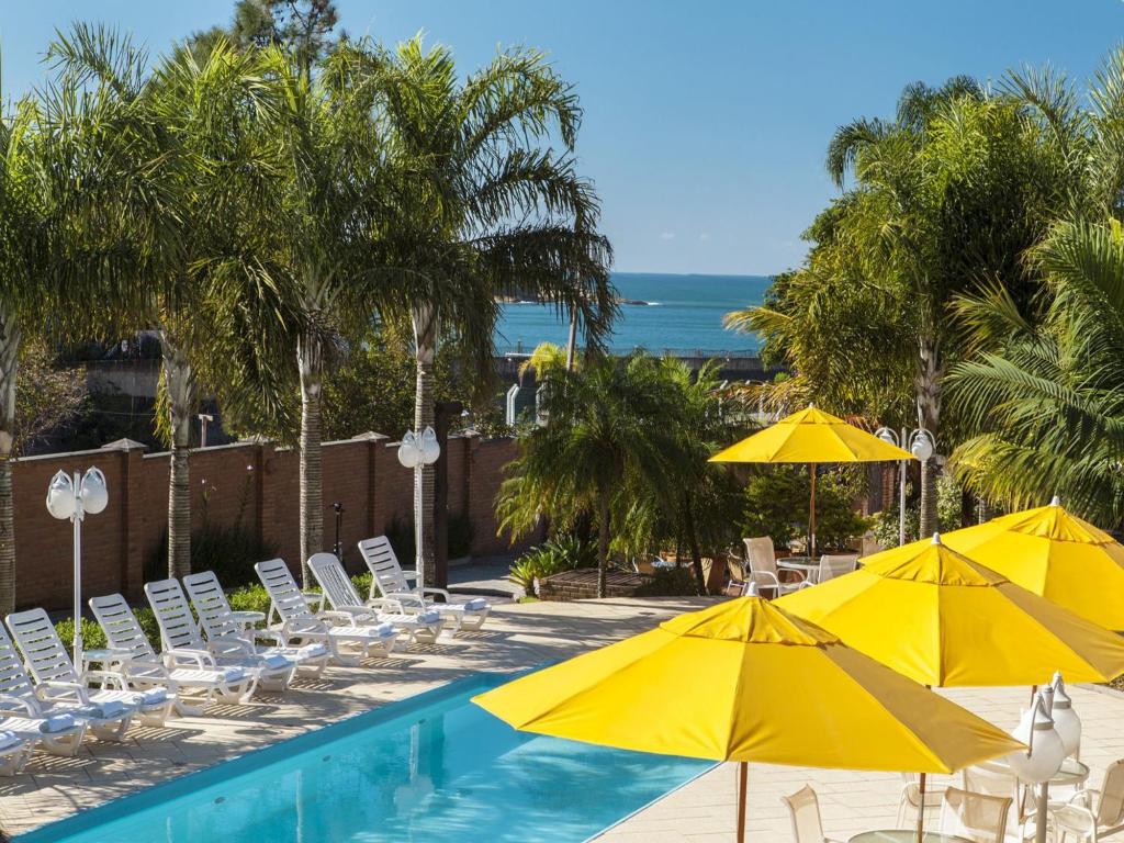 a pool with yellow umbrellas and chairs and the ocean at Pousada Ponta do Lobo in Balneário Camboriú