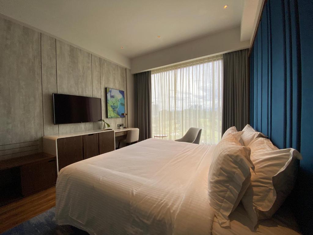 A bright bedroom with a large bed, television, desk, and full-height curtained window.