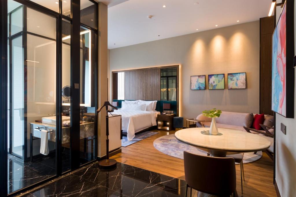 A spacious modern guest room with a bed, seating area, and dining table.