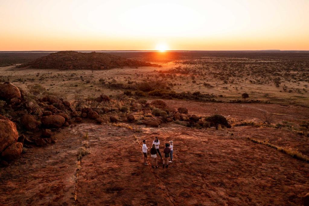 a group of three people walking down a dirt road at sunset at Wooleen Station in Wooleen