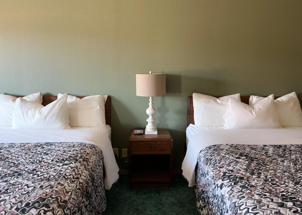 a hotel room with two beds and a lamp on a night stand at The Trail Inn - Sutton, Nebraska - US-6 HWY 
