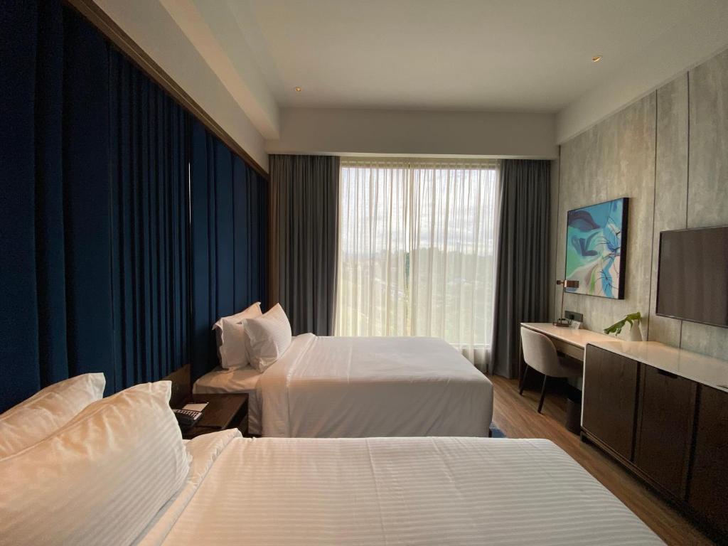 A twin room with two beds, a long desk and a full-height curtained window.