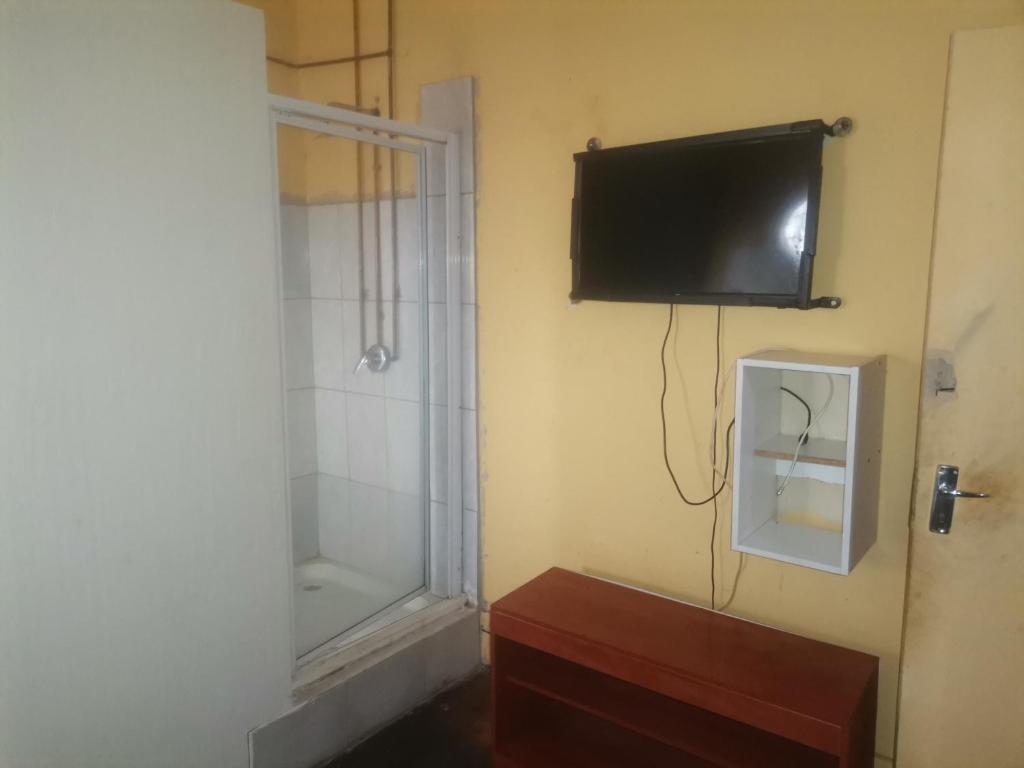 a bathroom with a shower and a television on the wall at New Dawn Guest House in Brakpan