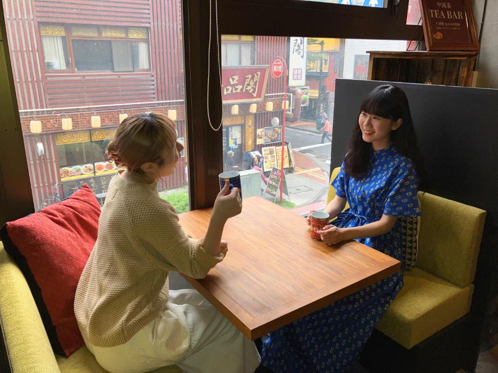 横浜市にあるHARE-TABI SAUNA&INN Yokohamaの二人の女性が携帯電話を見ながら テーブルに座っている