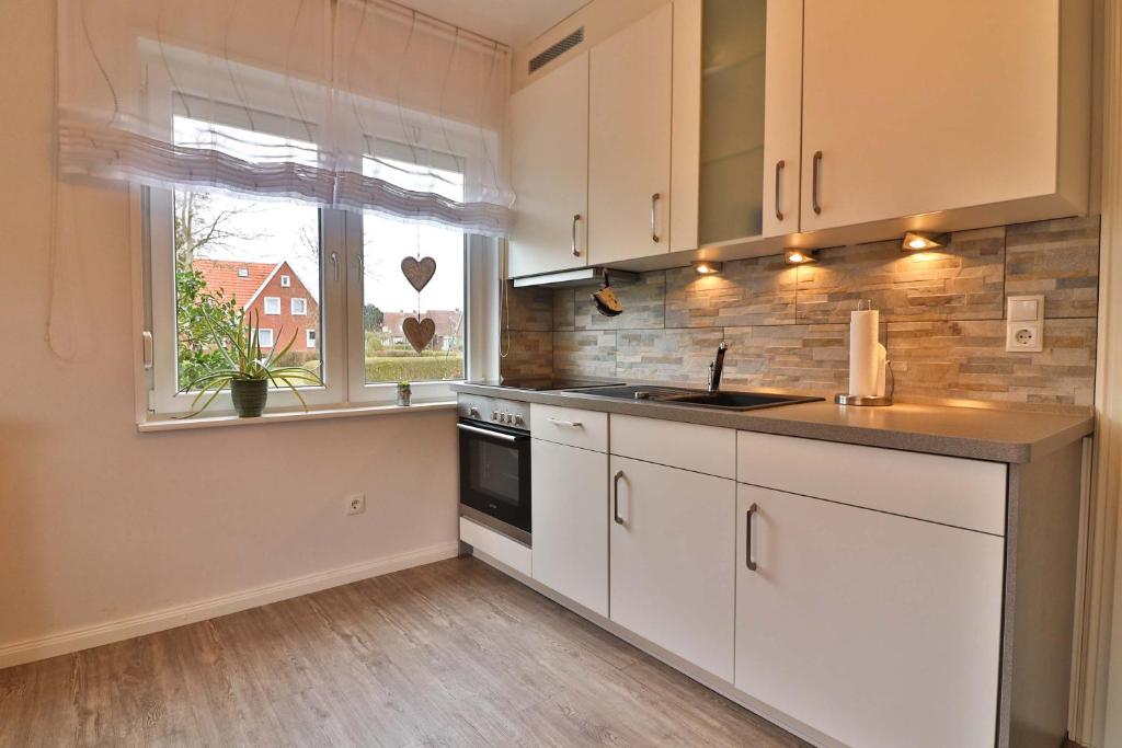 uma cozinha com armários brancos, um lavatório e uma janela em Kiek rin bi Kati - Ferienwohnung 1 em Langeoog