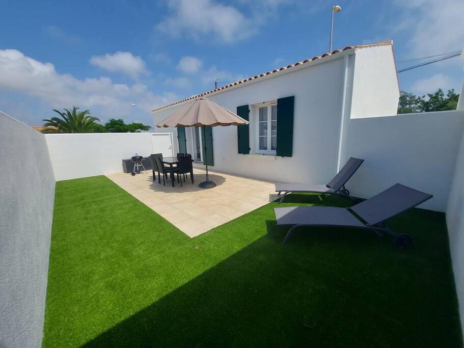 un patio con césped verde y una casa blanca en A tribord: maison chaleureuse à 5min de la plage, en La Cotinière