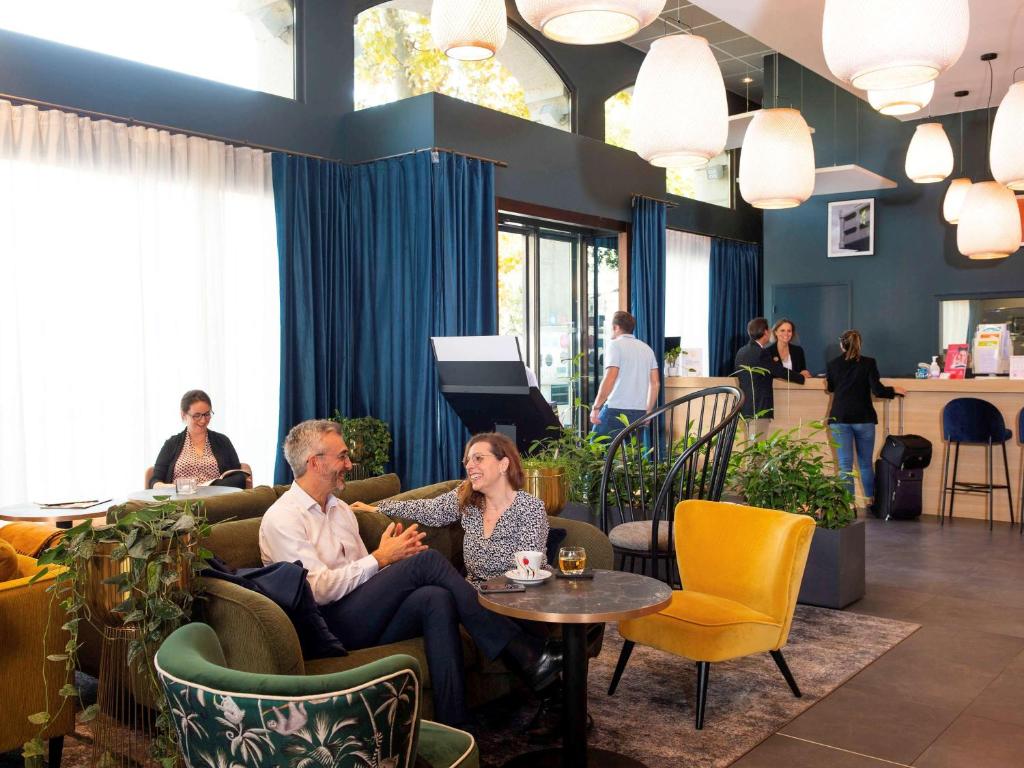 Ein Mann und eine Frau sitzen auf Sofas in der Lobby. in der Unterkunft Aparthotel Adagio Lyon Patio Confluence in Lyon