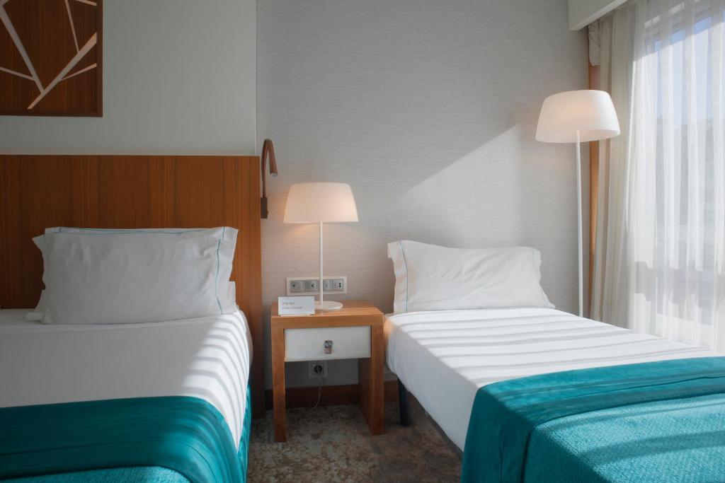 A bright twin room with two single beds, a shared bedside table, and a full-height glazed opening at the side.