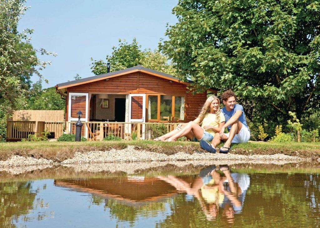 a man and a woman sitting next to a house next to a lake at Herons Brook Retreat Lodges in Narberth