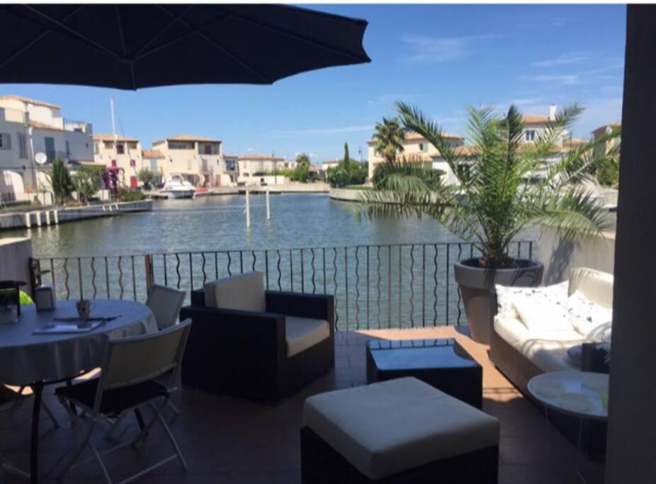 a balcony with a view of a river with tables and chairs at Marina Aigues Mortes 75m2 in Aigues-Mortes