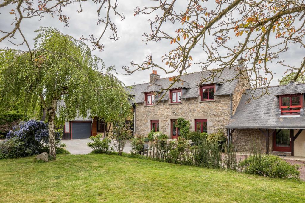 una antigua casa de piedra con ventanas rojas y un patio en LA VILLA DU GOLF - avec piscine couverte chauffée et jacuzzi, en Le Tronchet