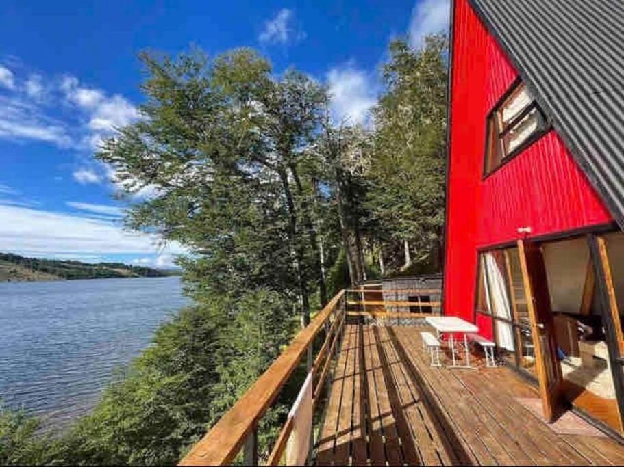 un edificio rosso con un ponte accanto a un corpo idrico di Refugio del Pollux- Coyhaique- Orillas Lago Pollux a Coihaique