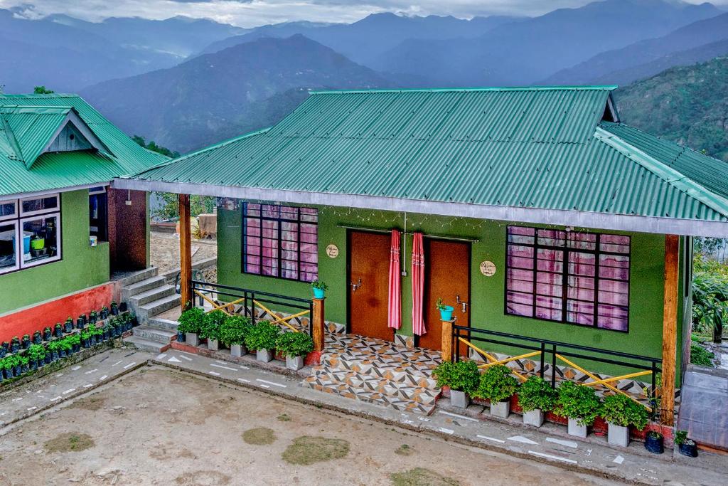 a green house with a red door and mountains in the background at 3 Sisters' Homestay in Ravangla
