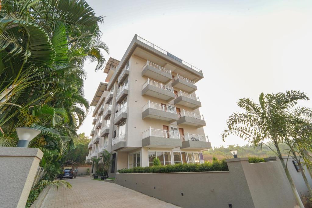 a tall white building with palm trees in front of it at Hotel Wayfarer in Porvorim