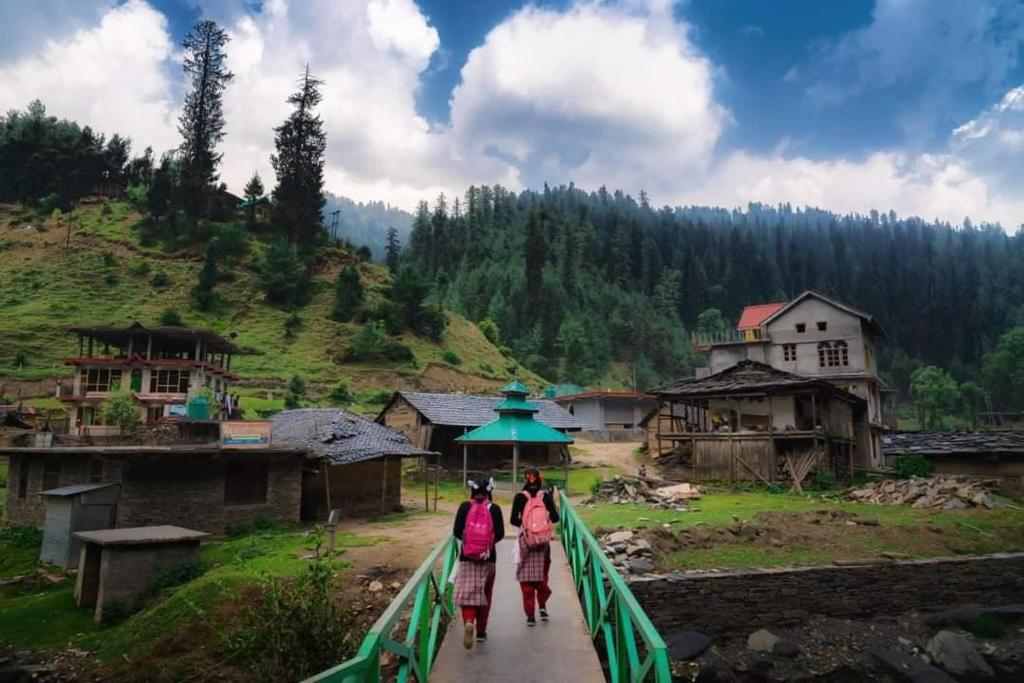 three people walking down a bridge in a village at Alpine Homestay at Gadagusain in Banjār