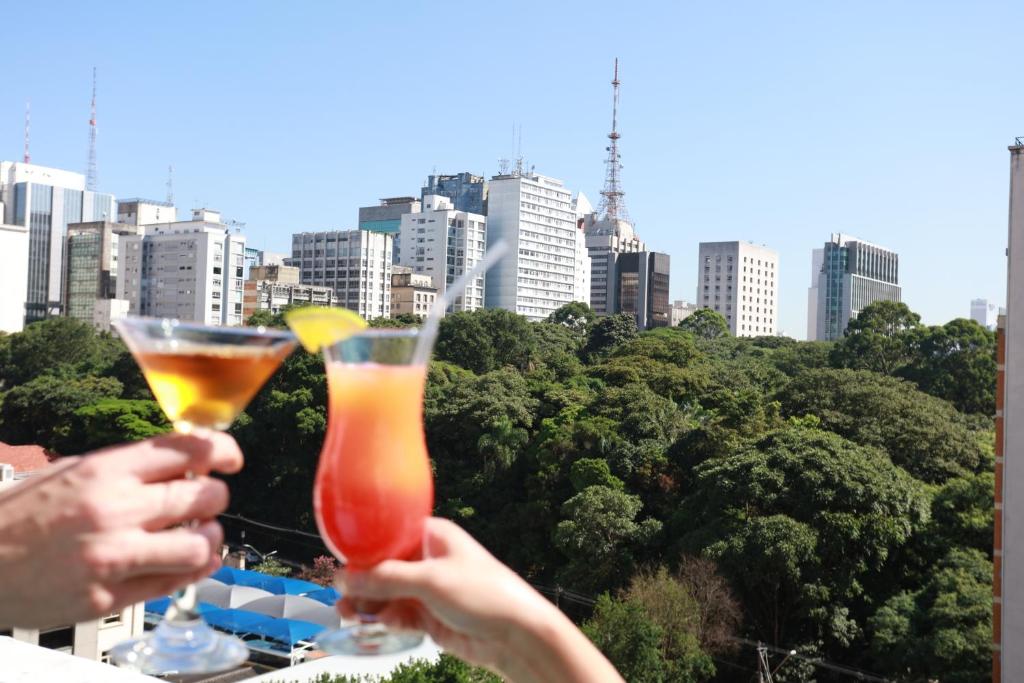 two people holding wine glasses with a city in the background at Hotel Trianon Paulista in Sao Paulo