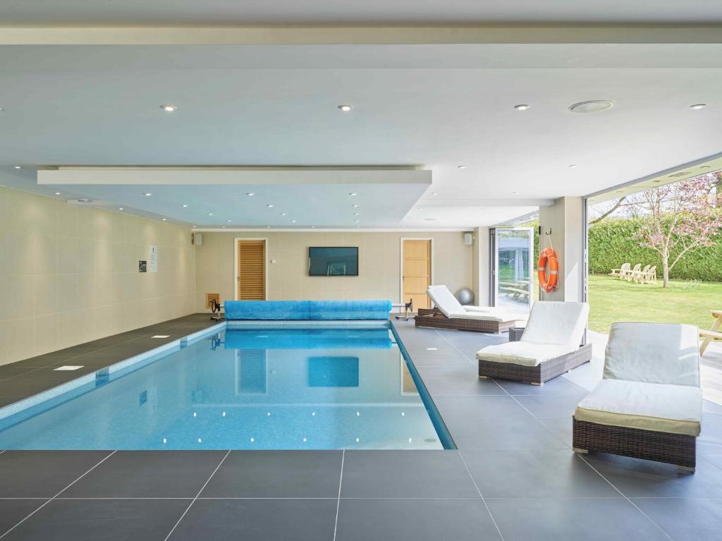 a swimming pool in a house with chairs and a couch at Cheltenham's Most Luxurious House in Charlton Kings