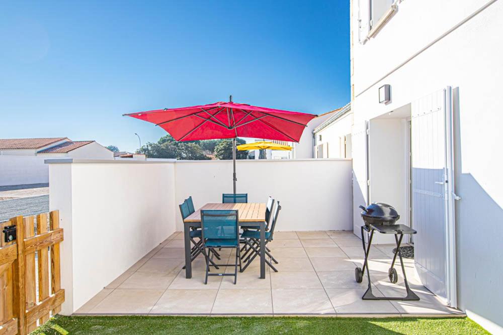 a patio with a table and chairs and a red umbrella at LE COMMODORE Maison avec piscine/parking/wifi/plages 5kms in Les Mathes