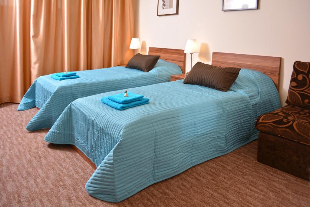 a room with two beds with blue sheets and a chair at Airport Glossel Panzió in Vecsés