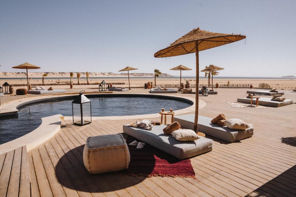 a pool with couches and umbrellas next to a beach at Caravan by Habitas Dakhla in Dakhla