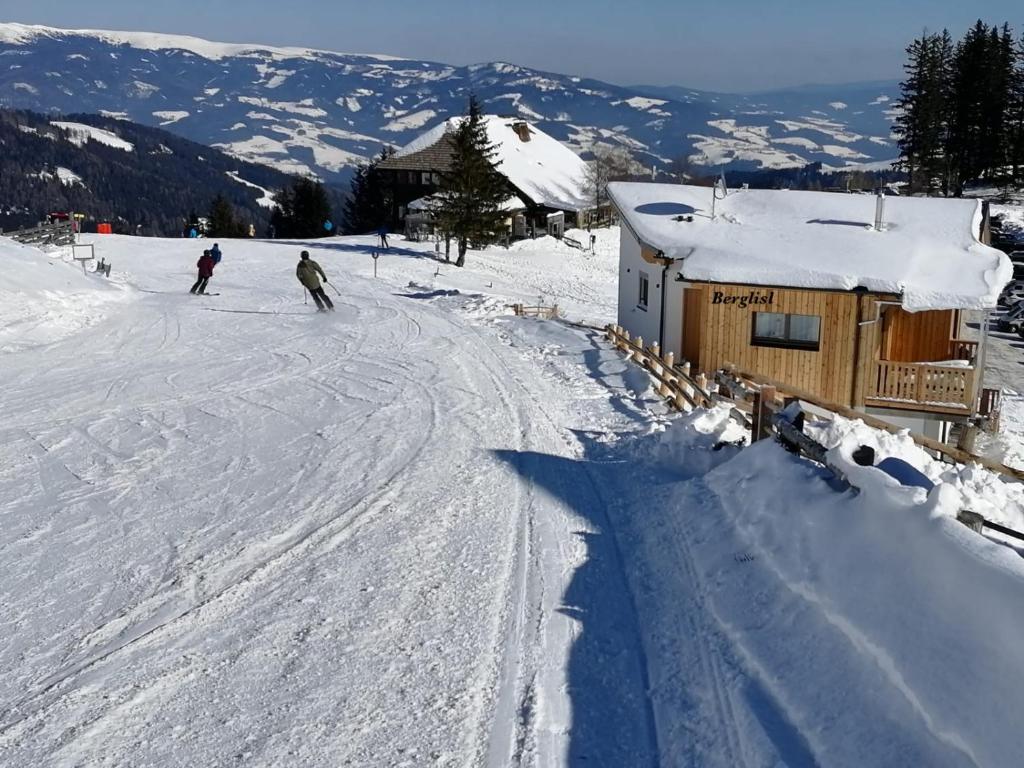 two people skiing down a snow covered slope next to a building at Berglisl - direkt an der Schipiste! Neue Ferienwohnung mit Sauna in Klippitztorl