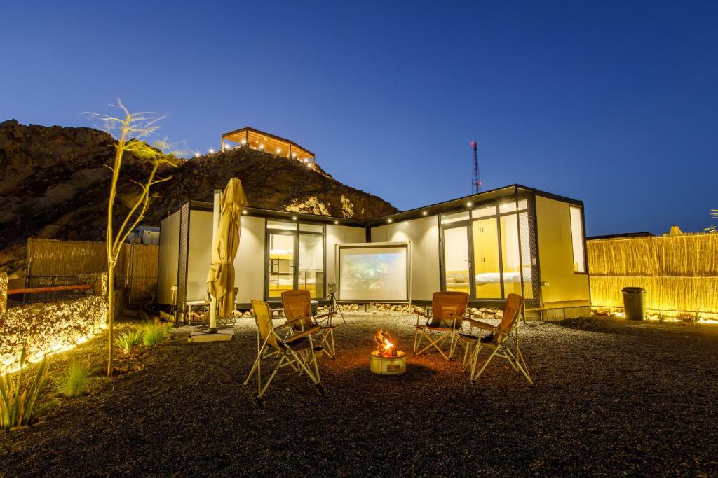 a house with chairs and a fire in front of it at Go Camp Mountain Nature Lodge مخيم الطبيعة الجبلية in Sharīyah