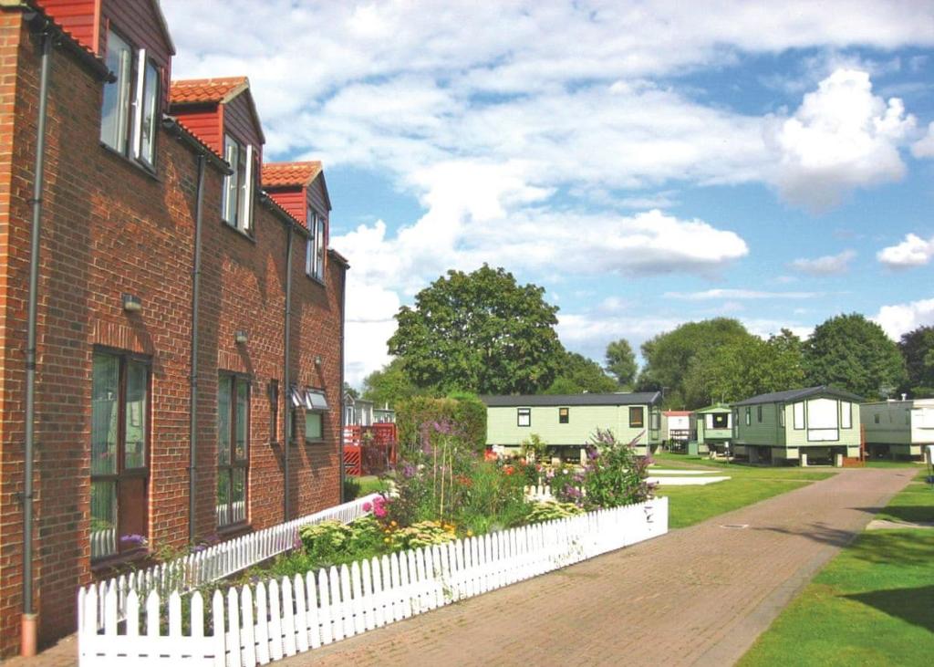 una casa de ladrillo con una valla blanca y flores en Weir Holiday Park, en Holtby