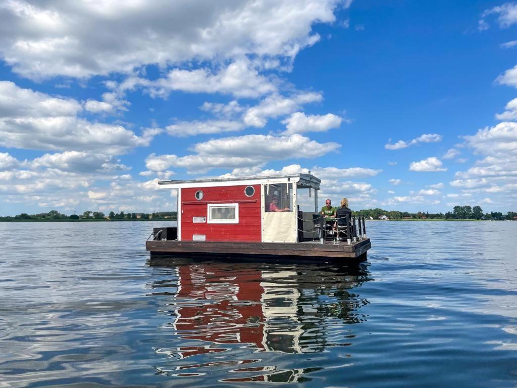 a small boat with a red house on the water at Hausfloßvermietung auf der Peene am Kummerower See in Mecklenburg Vorpommern in Dargun