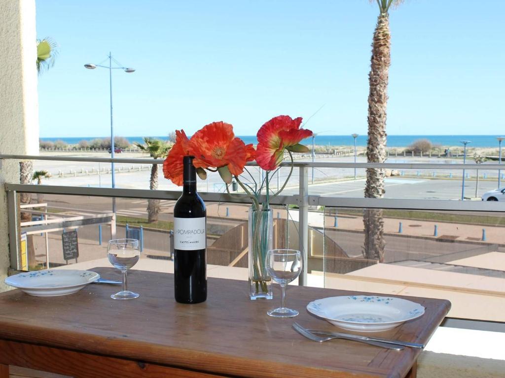 - une bouteille de vin et des verres sur une table avec des fleurs dans l'établissement Studio en Front de Mer à Saint-Pierre-la-Mer avec Loggia - 100m de la Plage, 200m du Centre - FR-1-229D-61, à Fleury
