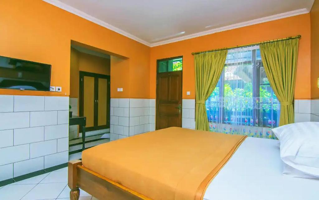 a bedroom with orange walls and a bed and a window at Kedin's Inn in Denpasar
