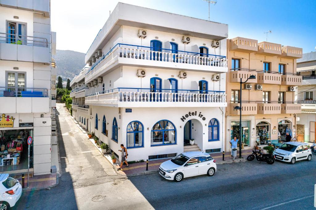 un edificio blanco alto con coches estacionados frente a él en Hotel Iro en Hersonissos