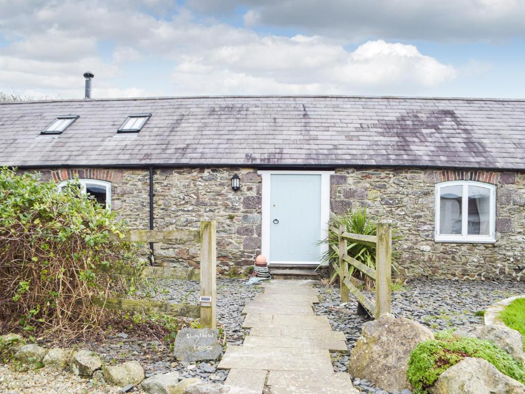 a stone cottage with a white door and a fence at Swallow Lodge in Mathry