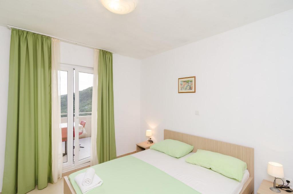 a bedroom with a bed with green curtains and a window at Apartments Feral in Saplunara