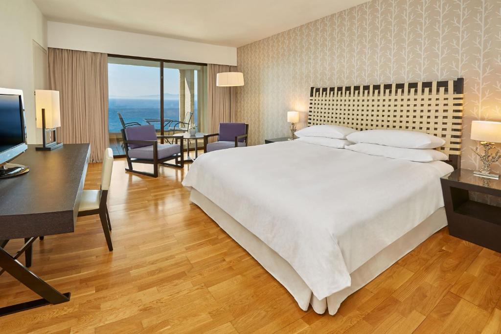 a bedroom with a large white bed and a desk at Sheraton Rhodes Resort in Ixia