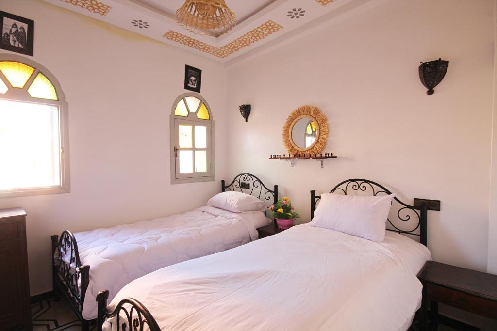 two beds in a room with white walls and a mirror at Araf House in Marrakesh